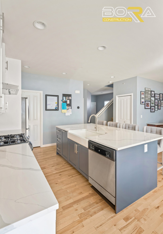 Inspiration for a mid-sized single-wall light wood floor and brown floor eat-in kitchen remodel in Seattle with a farmhouse sink, shaker cabinets, white cabinets, quartz countertops, white backsplash, quartz backsplash, stainless steel appliances, an island and white countertops