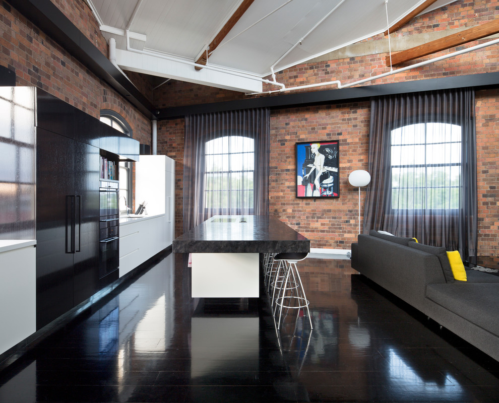 This is an example of a mid-sized industrial open plan kitchen in Brisbane with dark hardwood floors, with island, flat-panel cabinets, white cabinets, black floor, an undermount sink, marble benchtops and black appliances.