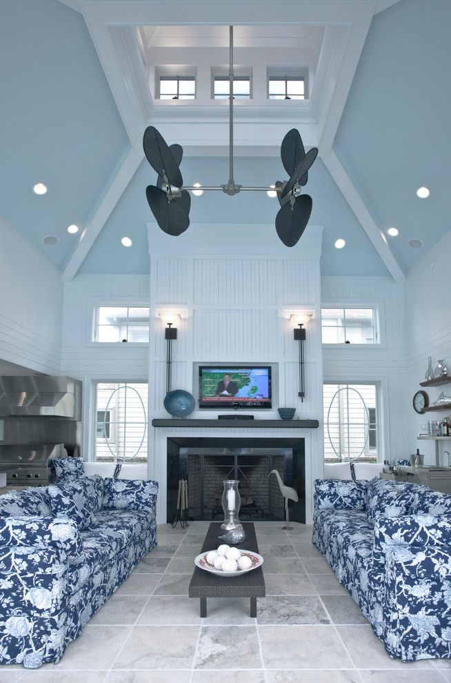 This is an example of a large beach style open concept living room in Baltimore with blue walls, limestone floors, a standard fireplace, a stone fireplace surround, a wall-mounted tv and grey floor.