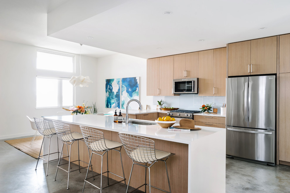Inspiration for a mid-sized beach style l-shaped eat-in kitchen in Austin with flat-panel cabinets, light wood cabinets, quartzite benchtops, white splashback, stainless steel appliances, concrete floors, with island, grey floor, an undermount sink and glass sheet splashback.