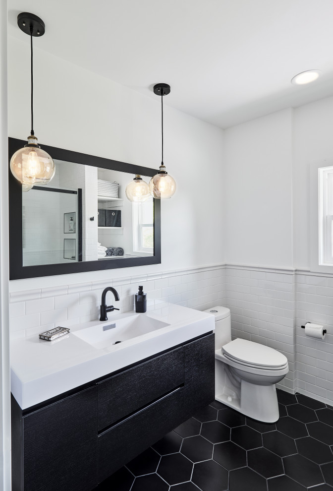 Inspiration for a mid-sized transitional bathroom in Portland with flat-panel cabinets, black cabinets, an alcove shower, a two-piece toilet, white tile, subway tile, white walls, ceramic floors, an integrated sink, engineered quartz benchtops, black floor, a sliding shower screen and white benchtops.