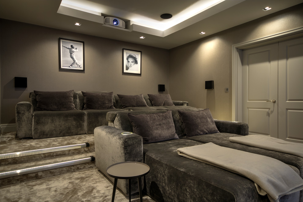 Photo of a large transitional enclosed home theatre in Kent with brown walls, carpet, a projector screen and beige floor.