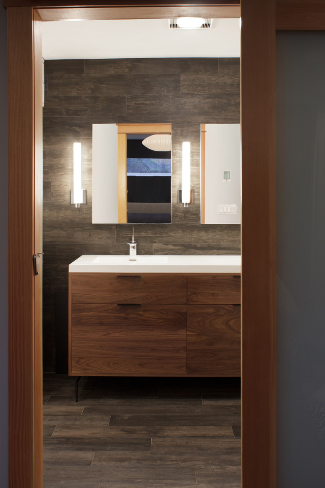 Photo of a small modern bathroom in New York with flat-panel cabinets, medium wood cabinets, a drop-in tub, a shower/bathtub combo, a two-piece toilet, white tile, porcelain tile, beige walls, medium hardwood floors, an integrated sink and solid surface benchtops.
