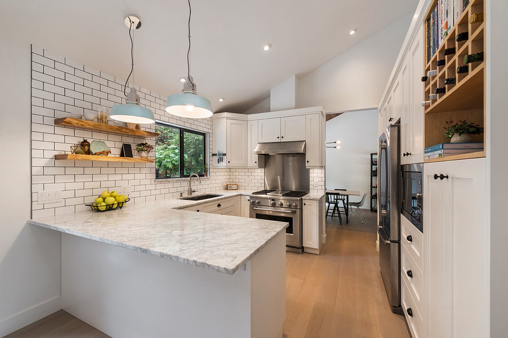 Photo of a mid-sized transitional u-shaped separate kitchen in Vancouver with an undermount sink, shaker cabinets, white cabinets, marble benchtops, white splashback, subway tile splashback, stainless steel appliances, light hardwood floors, a peninsula, beige floor and grey benchtop.