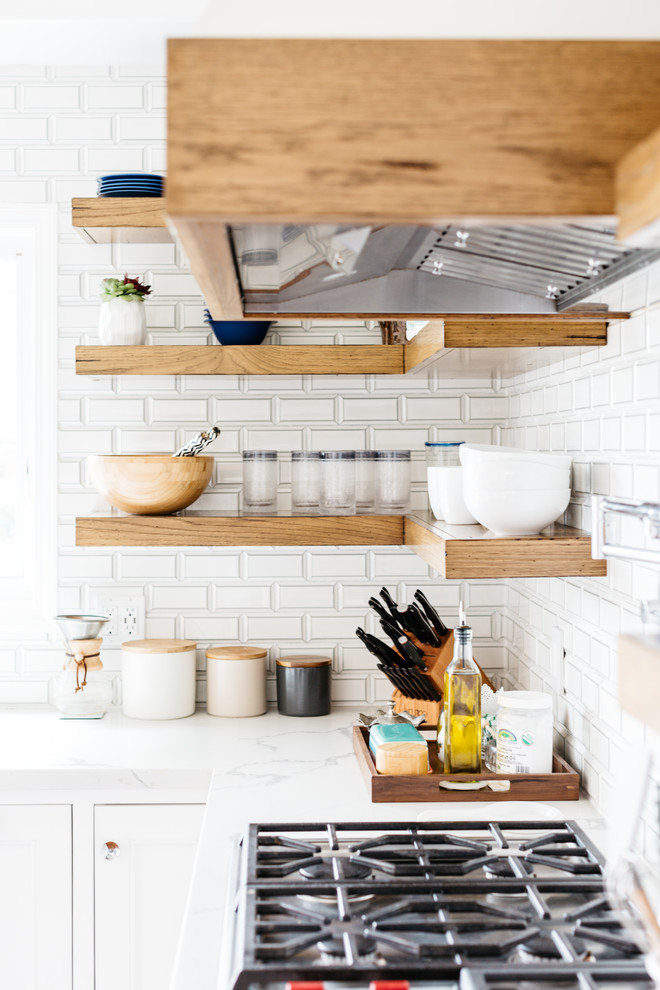 Example of a mid-sized transitional u-shaped medium tone wood floor and brown floor eat-in kitchen design in Los Angeles with a farmhouse sink, recessed-panel cabinets, white cabinets, quartzite countertops, white backsplash, subway tile backsplash, stainless steel appliances, an island and white countertops