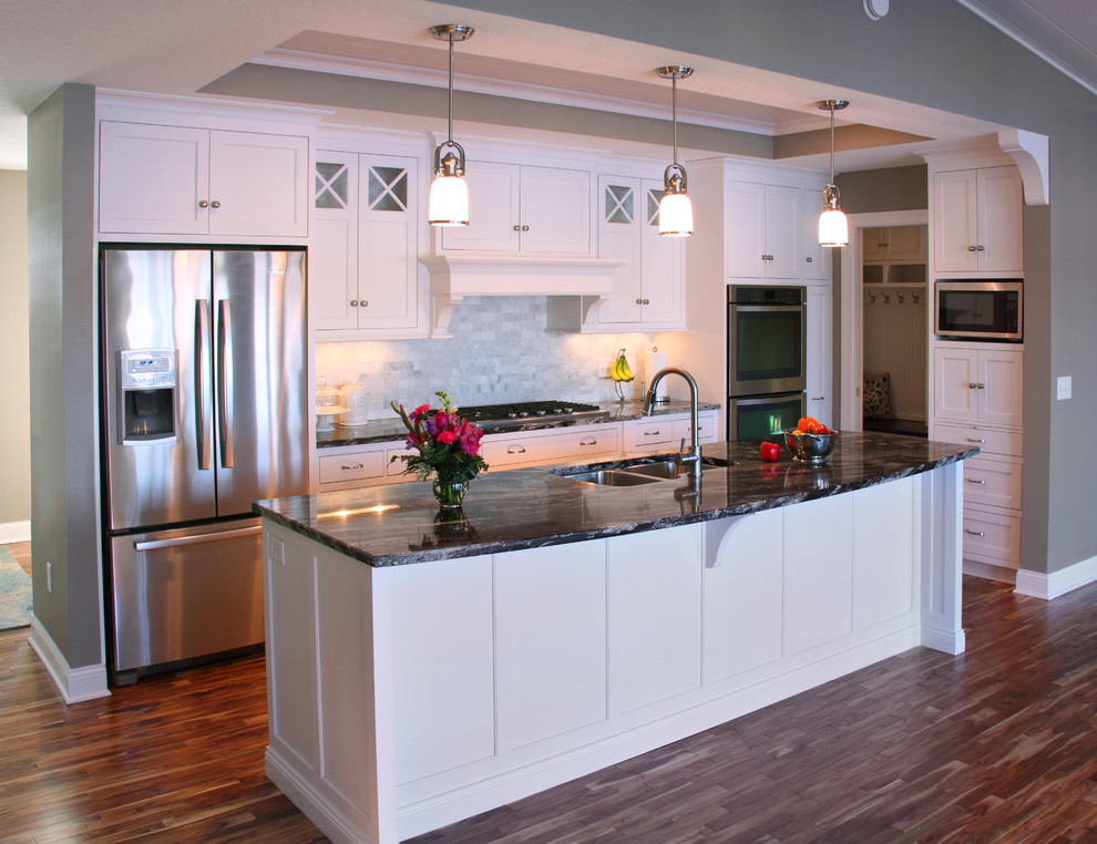 Mid-sized elegant galley medium tone wood floor open concept kitchen photo in Minneapolis with an undermount sink, shaker cabinets, white cabinets, granite countertops, white backsplash, stone tile backsplash, stainless steel appliances and an island