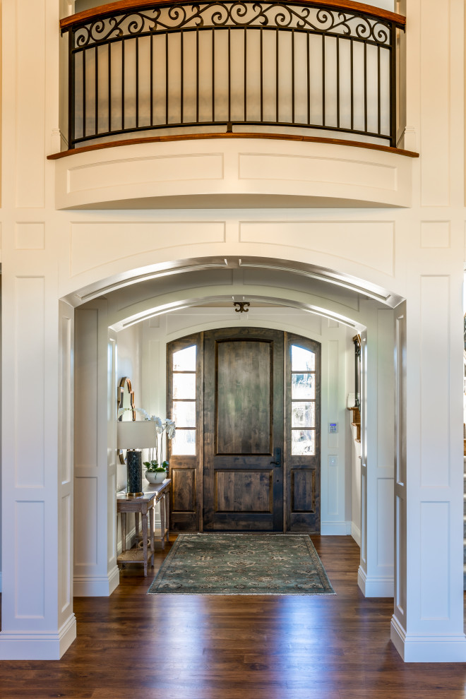 Cette image montre une grande porte d'entrée traditionnelle avec un mur beige, un sol en bois brun, une porte simple, une porte en bois foncé, un sol multicolore et un plafond voûté.