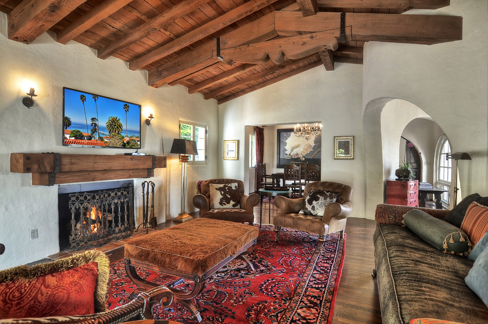 Photo of an expansive mediterranean open concept family room in Orange County with white walls, dark hardwood floors, a two-sided fireplace, a plaster fireplace surround and a wall-mounted tv.