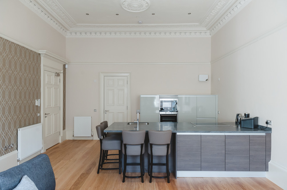 This is an example of a contemporary open plan kitchen in Glasgow with an undermount sink, flat-panel cabinets, grey cabinets, panelled appliances, light hardwood floors and with island.