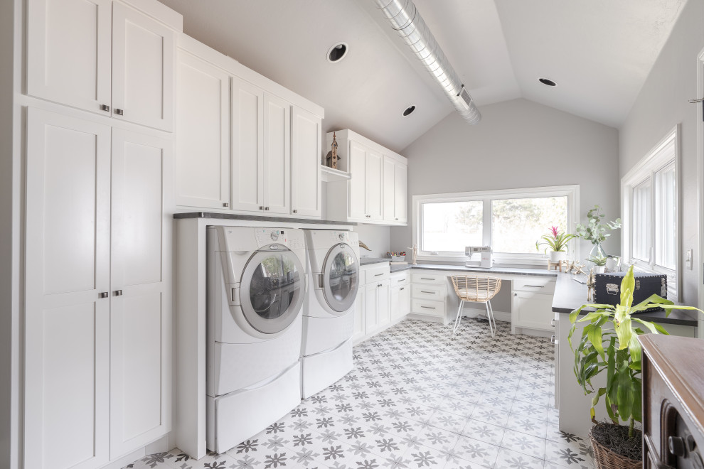Design ideas for a mid-sized beach style laundry room in Oklahoma City with a farmhouse sink, shaker cabinets, blue cabinets, soapstone benchtops, marble splashback, medium hardwood floors and grey benchtop.