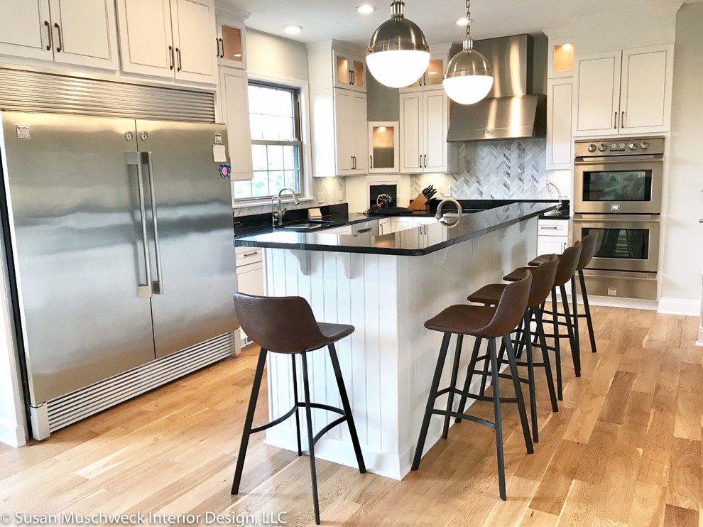 Open concept kitchen - large transitional u-shaped light wood floor open concept kitchen idea with an undermount sink, raised-panel cabinets, white cabinets, granite countertops, multicolored backsplash, marble backsplash, stainless steel appliances, an island and black countertops
