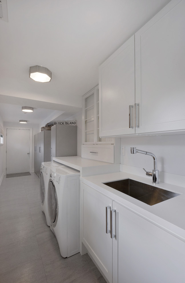 Design ideas for a large modern single-wall dedicated laundry room in New York with an undermount sink, recessed-panel cabinets, white cabinets, solid surface benchtops, white walls, porcelain floors and a side-by-side washer and dryer.