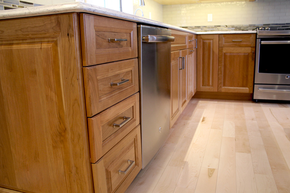 Inspiration for a large transitional u-shaped light wood floor and beige floor home design remodel in Boston with an undermount sink, raised-panel cabinets, medium tone wood cabinets, quartz countertops, multicolored backsplash, glass tile backsplash, stainless steel appliances, an island and beige countertops