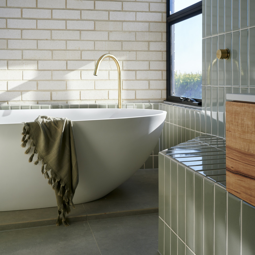 Photo of a mid-sized contemporary master wet room bathroom in Adelaide with flat-panel cabinets, medium wood cabinets, a freestanding tub, a one-piece toilet, green tile, ceramic tile, green walls, ceramic floors, a vessel sink, engineered quartz benchtops, grey floor, an open shower and white benchtops.