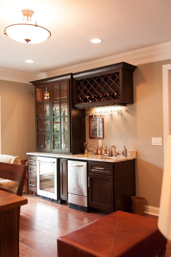 Small traditional single-wall wet bar in Other with an undermount sink, dark wood cabinets, granite benchtops, multi-coloured splashback and medium hardwood floors.