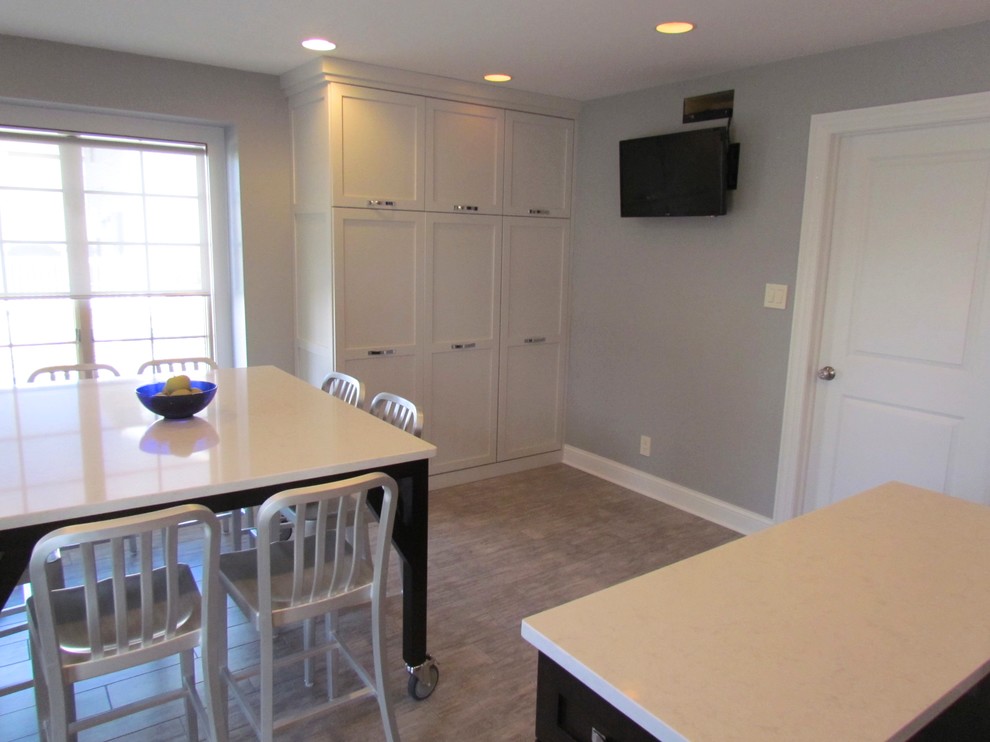 Example of a transitional l-shaped porcelain tile eat-in kitchen design in Chicago with a farmhouse sink, shaker cabinets, white cabinets, quartz countertops, blue backsplash, glass tile backsplash, stainless steel appliances and an island