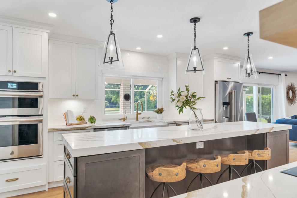 Open concept kitchen - large transitional medium tone wood floor and brown floor open concept kitchen idea in Miami with a farmhouse sink, shaker cabinets, white cabinets, quartz countertops, white backsplash, subway tile backsplash, stainless steel appliances, an island and white countertops