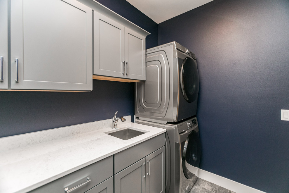 Design ideas for a transitional single-wall utility room in Cedar Rapids with grey cabinets, blue walls and a stacked washer and dryer.