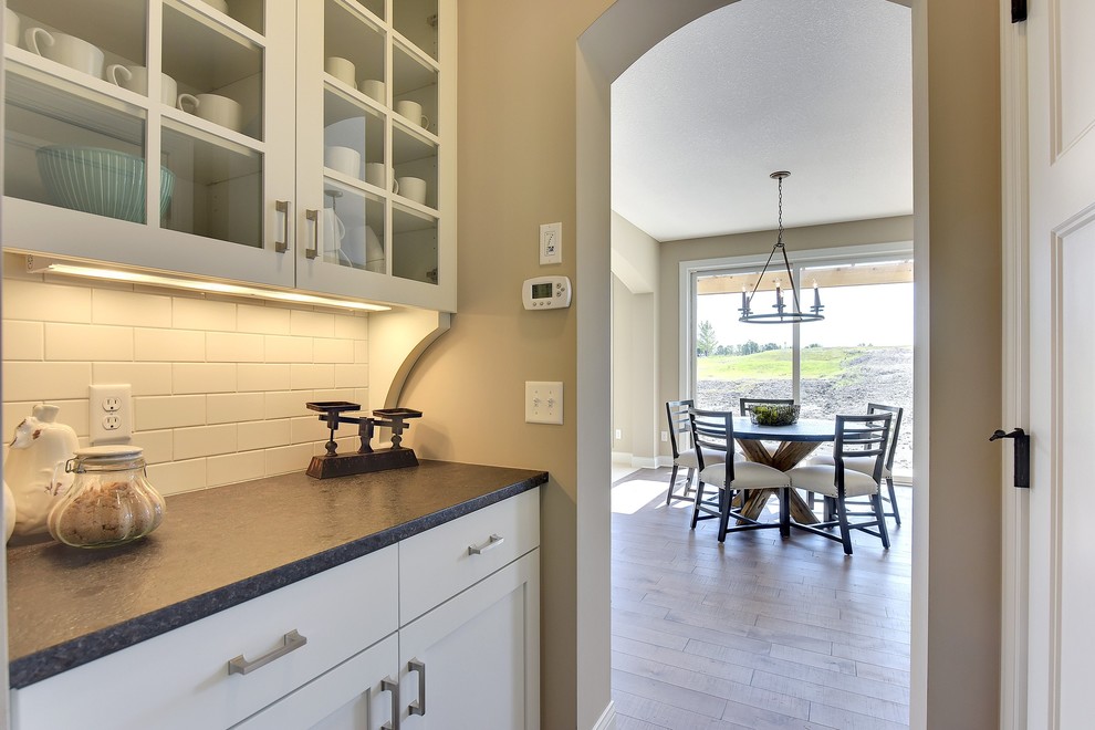 This is an example of a large transitional galley kitchen pantry in Minneapolis with glass-front cabinets, white cabinets, white splashback, subway tile splashback and with island.
