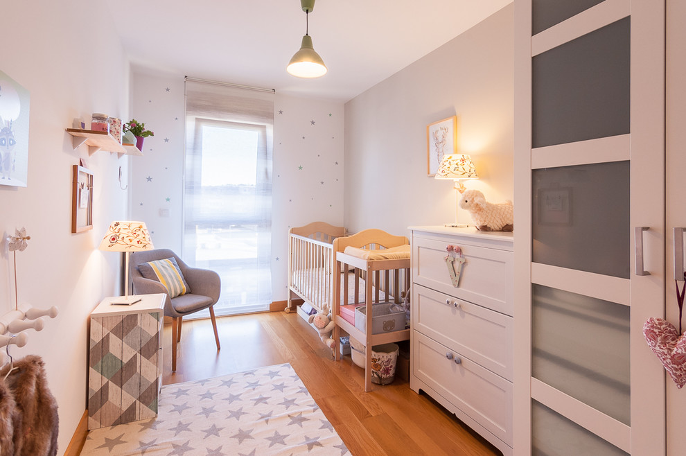 Imagen de habitación de bebé contemporánea con paredes blancas, suelo de madera en tonos medios y suelo marrón