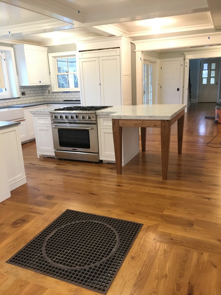 This is an example of a mid-sized country u-shaped eat-in kitchen in Bridgeport with a farmhouse sink, recessed-panel cabinets, white cabinets, marble benchtops, white splashback, subway tile splashback, stainless steel appliances, medium hardwood floors and with island.