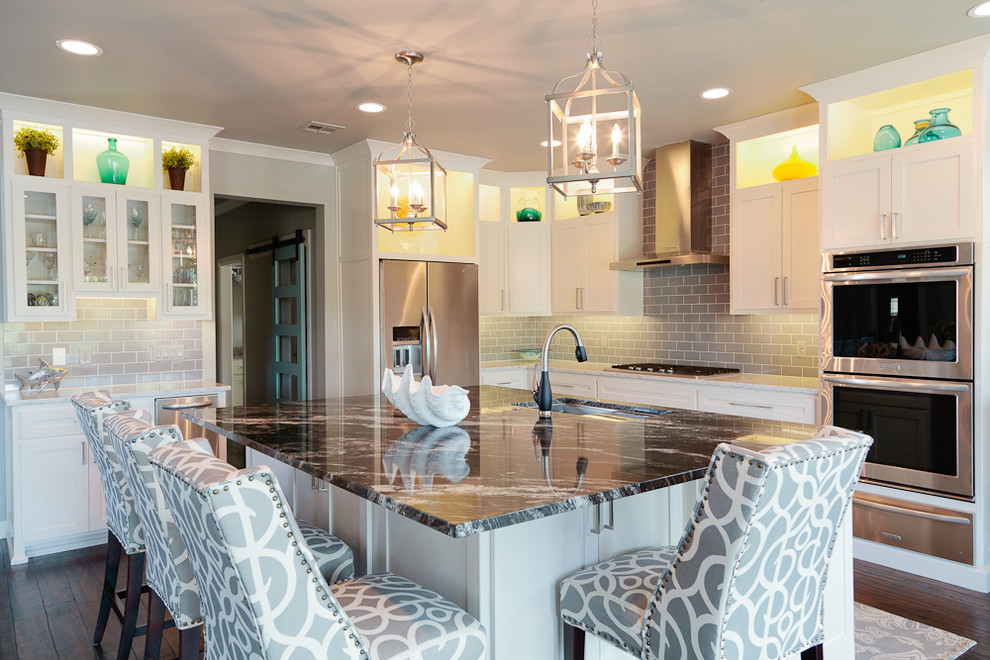Inspiration for a mid-sized coastal u-shaped dark wood floor eat-in kitchen remodel with an undermount sink, shaker cabinets, white cabinets, granite countertops, gray backsplash, glass tile backsplash, stainless steel appliances and an island