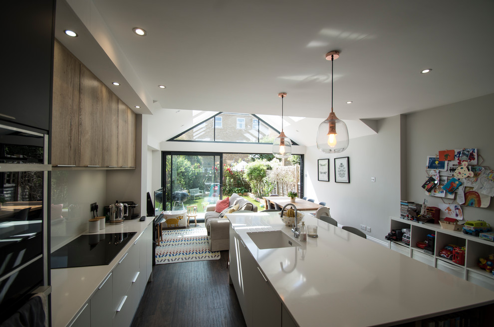 Small modern open plan kitchen with an integrated sink, flat-panel cabinets, white cabinets, solid surface benchtops, white splashback, glass sheet splashback, stainless steel appliances, plywood floors, with island, brown floor and white benchtop.