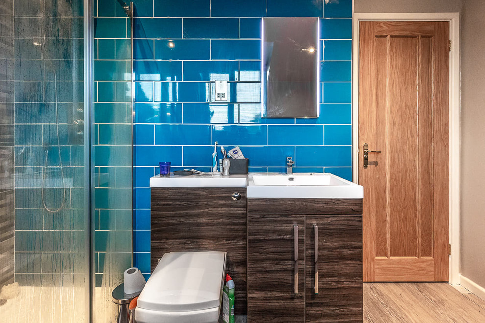 Modern master bathroom in Cardiff with brown cabinets, a corner shower, blue tile, blue walls, brown floor, a hinged shower door, a freestanding tub and a one-piece toilet.