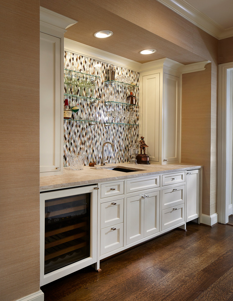 Inspiration for a mid-sized traditional single-wall wet bar in Dallas with an undermount sink, white cabinets, marble benchtops, multi-coloured splashback, recessed-panel cabinets, mosaic tile splashback, dark hardwood floors, brown floor and beige benchtop.