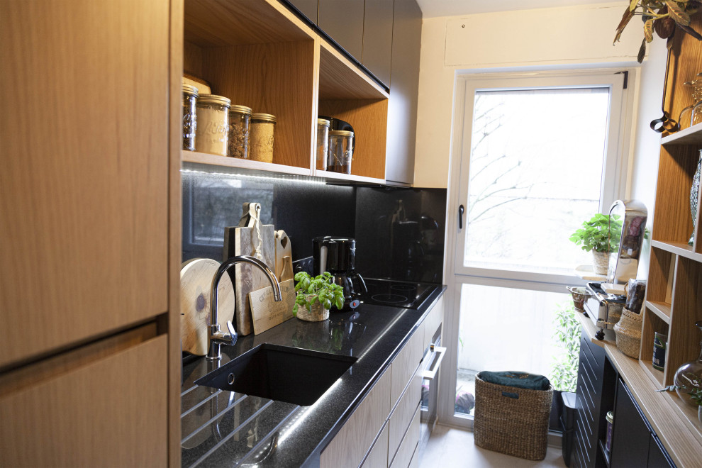 This is an example of a small contemporary single-wall separate kitchen in Paris with an integrated sink, beaded inset cabinets, black cabinets, granite benchtops, black splashback, granite splashback, grey floor and black benchtop.
