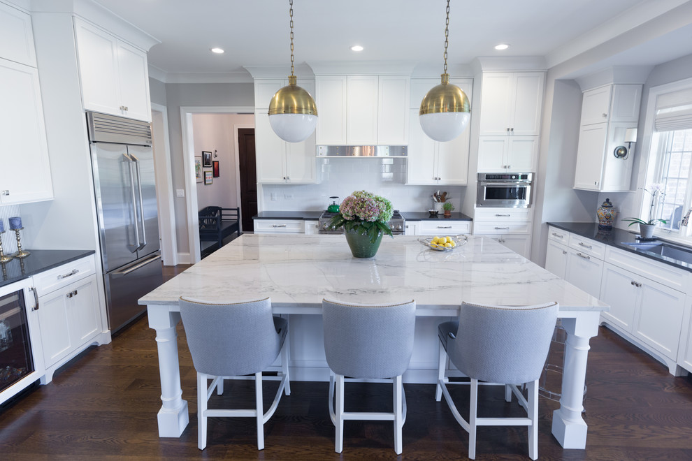 Inspiration for a large transitional u-shaped dark wood floor and brown floor kitchen remodel in Chicago with an undermount sink, shaker cabinets, white cabinets, solid surface countertops, white backsplash, ceramic backsplash, stainless steel appliances, an island and black countertops