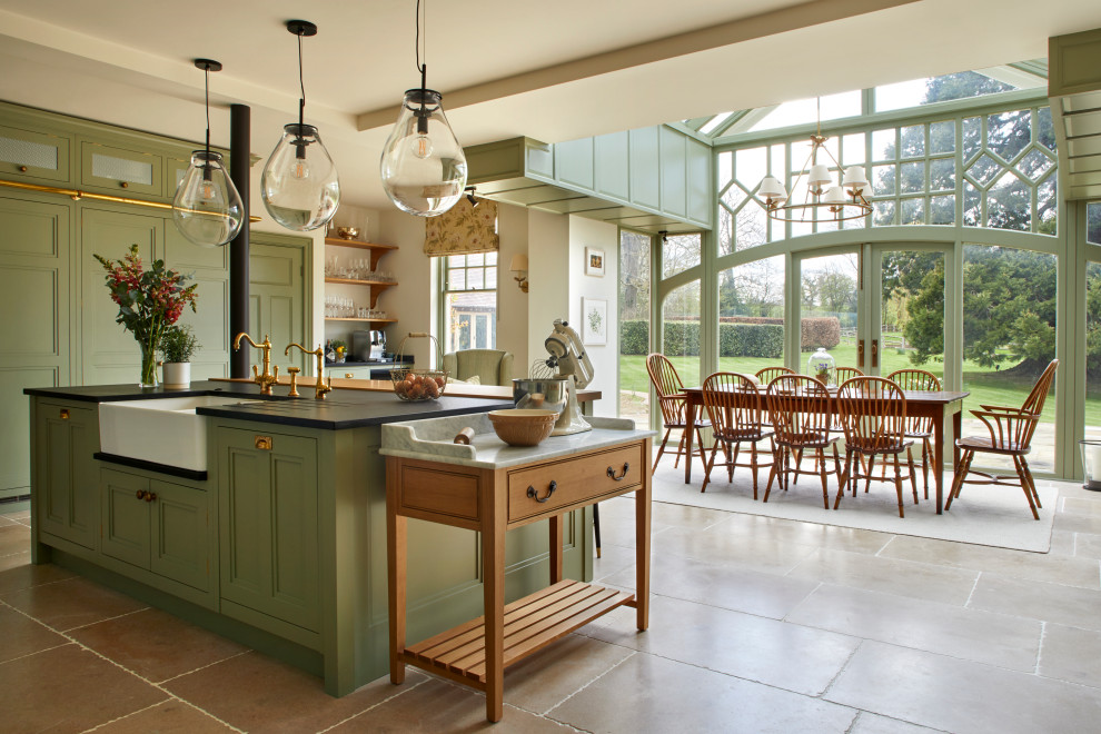 Design ideas for an expansive country u-shaped eat-in kitchen in London with a farmhouse sink, recessed-panel cabinets, green cabinets, granite benchtops, green splashback, ceramic splashback, panelled appliances, limestone floors, with island, beige floor and black benchtop.