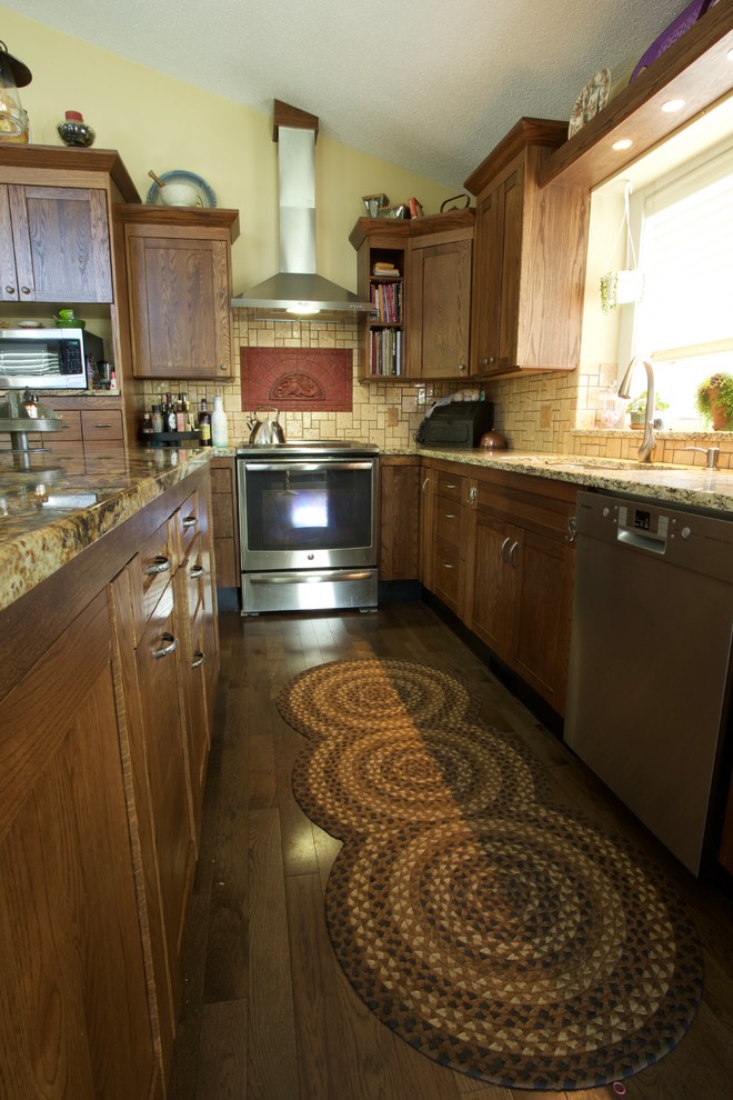 Large transitional l-shaped dark wood floor and brown floor kitchen photo in Calgary with an undermount sink, shaker cabinets, medium tone wood cabinets, granite countertops, beige backsplash, ceramic backsplash, stainless steel appliances and an island