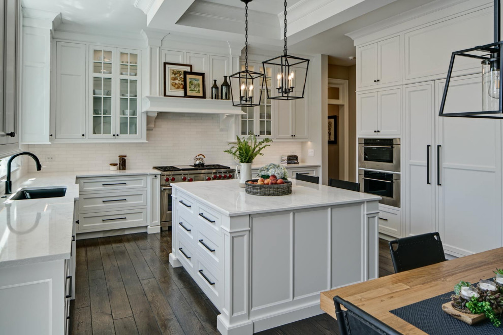 Example of a transitional l-shaped dark wood floor, brown floor and tray ceiling eat-in kitchen design in Chicago with an undermount sink, recessed-panel cabinets, white cabinets, quartzite countertops, white backsplash, ceramic backsplash, stainless steel appliances, an island and white countertops