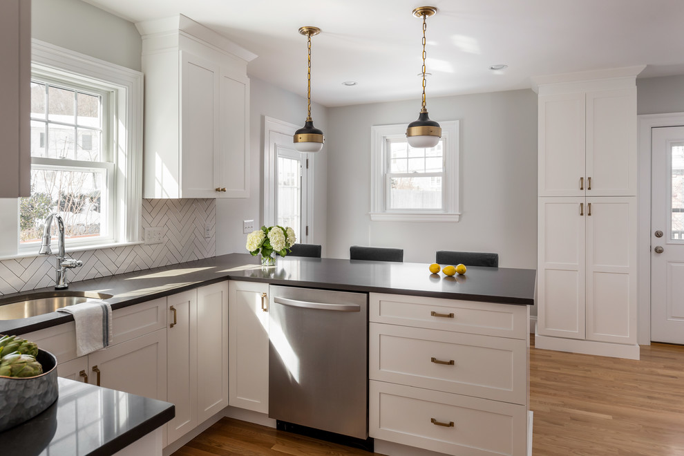 Example of a mid-sized transitional u-shaped light wood floor and brown floor enclosed kitchen design in Boston with an undermount sink, shaker cabinets, white cabinets, quartz countertops, gray backsplash, ceramic backsplash, stainless steel appliances, a peninsula and gray countertops