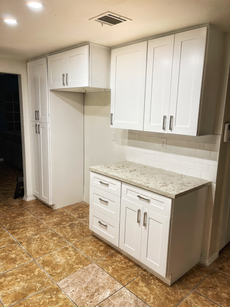 Photo of a large transitional u-shaped open plan kitchen in Los Angeles with an undermount sink, shaker cabinets, white cabinets, quartz benchtops, white splashback, porcelain splashback, stainless steel appliances, travertine floors, no island, brown floor and multi-coloured benchtop.