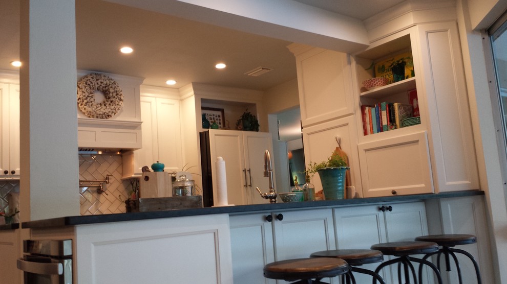 Example of a transitional galley kitchen design in Tampa with a farmhouse sink, recessed-panel cabinets, white cabinets, granite countertops, beige backsplash, glass tile backsplash, paneled appliances and an island