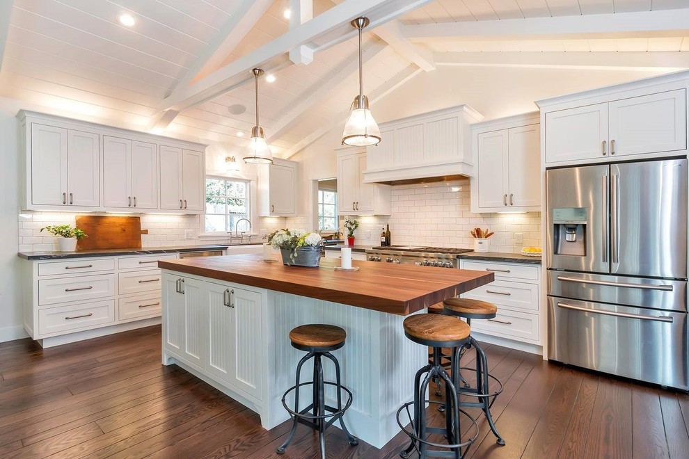 Inspiration for a large country l-shaped eat-in kitchen in San Francisco with a farmhouse sink, white splashback, subway tile splashback, stainless steel appliances, dark hardwood floors, brown floor, beaded inset cabinets, white cabinets, soapstone benchtops, with island and black benchtop.