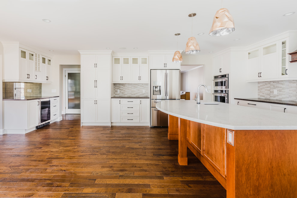 Example of a mid-sized transitional u-shaped medium tone wood floor open concept kitchen design in Calgary with an undermount sink, recessed-panel cabinets, white cabinets, quartz countertops, gray backsplash, ceramic backsplash, stainless steel appliances and an island