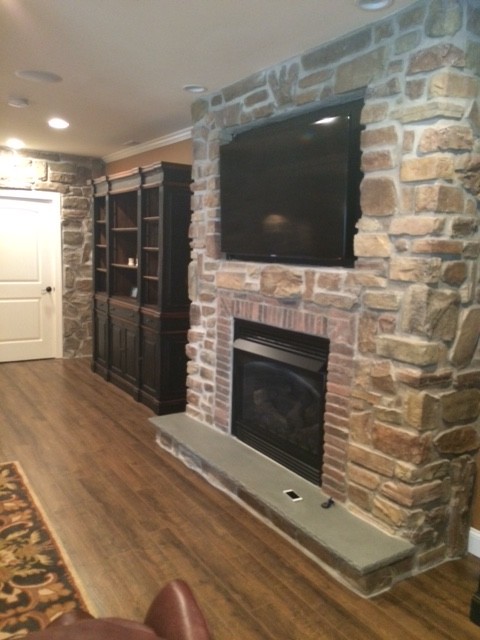 Photo of a large transitional walk-out basement in Philadelphia with beige walls, medium hardwood floors, a standard fireplace and a brick fireplace surround.