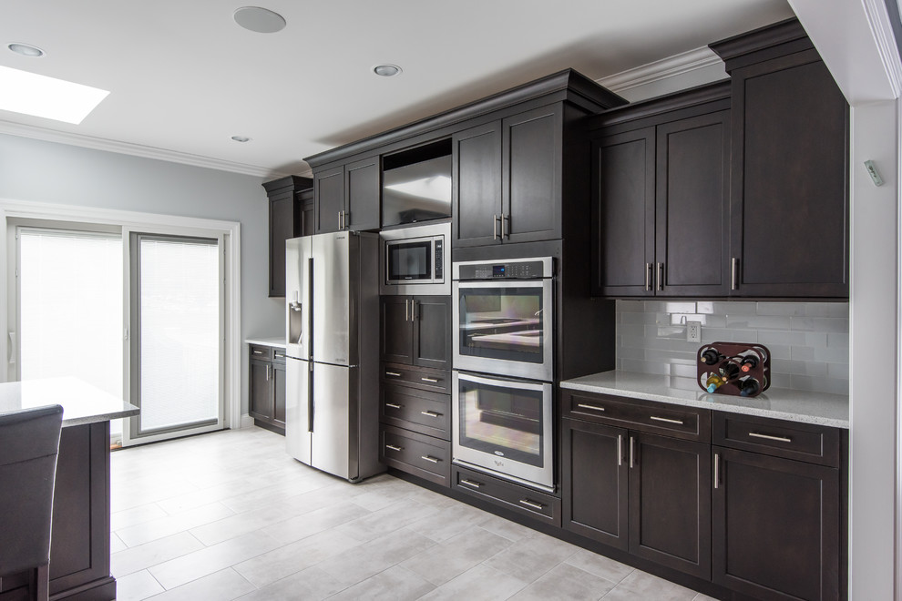 Design ideas for a large traditional l-shaped eat-in kitchen in Atlanta with an undermount sink, shaker cabinets, dark wood cabinets, granite benchtops, white splashback, glass tile splashback, stainless steel appliances, ceramic floors and with island.