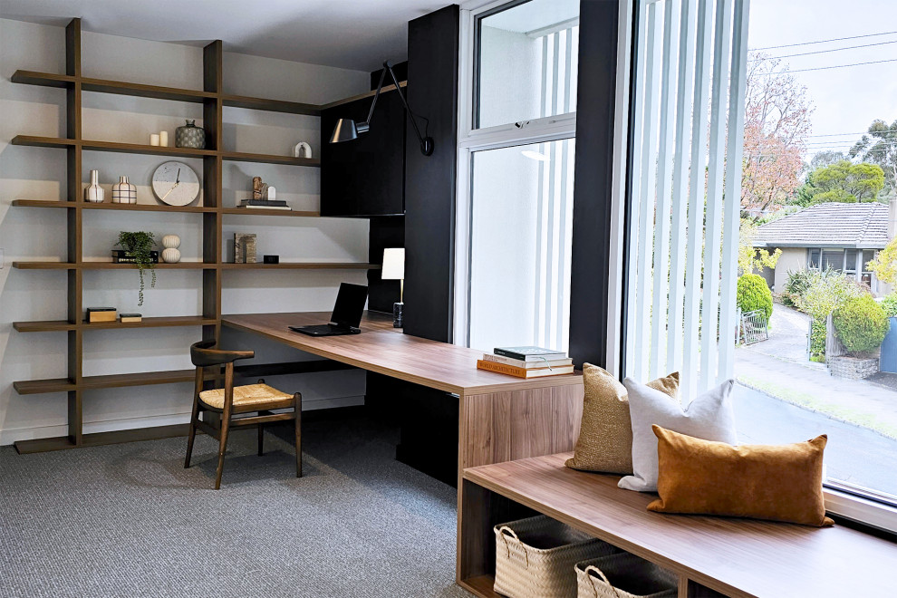 Cette image montre un bureau design de taille moyenne avec une bibliothèque ou un coin lecture, un mur blanc, moquette, un bureau intégré et un sol gris.