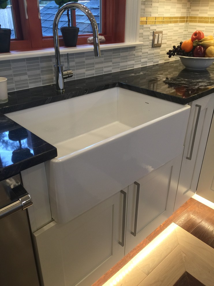 Example of a mid-sized transitional u-shaped light wood floor and beige floor eat-in kitchen design in Boston with a farmhouse sink, granite countertops, stainless steel appliances, an island, recessed-panel cabinets, white cabinets, beige backsplash, stone tile backsplash and multicolored countertops