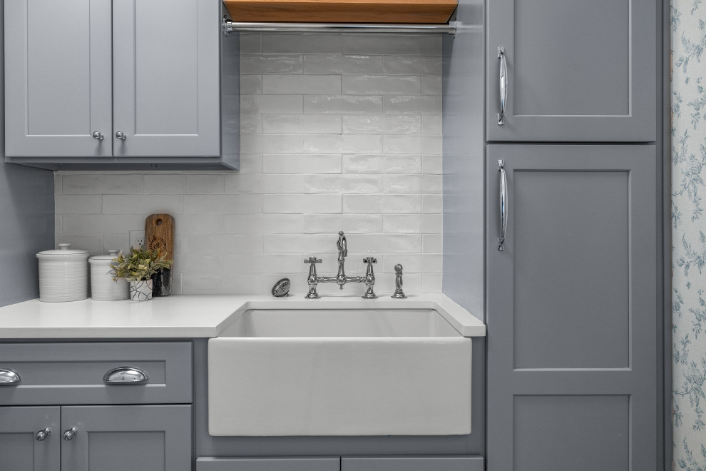 This is an example of a mid-sized transitional dedicated laundry room in Atlanta with a farmhouse sink, shaker cabinets, grey cabinets, quartz benchtops, white splashback, subway tile splashback, multi-coloured walls, marble floors, a stacked washer and dryer, multi-coloured floor, white benchtop and wallpaper.