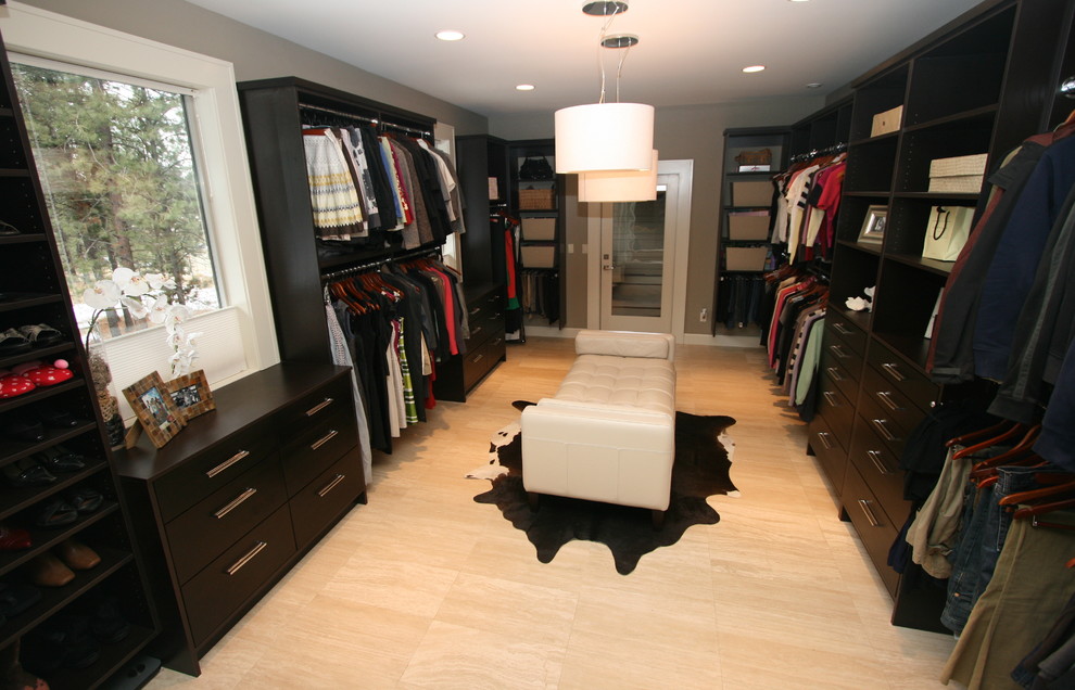 Photo of a large contemporary gender-neutral walk-in wardrobe in Seattle with flat-panel cabinets, dark wood cabinets and travertine floors.