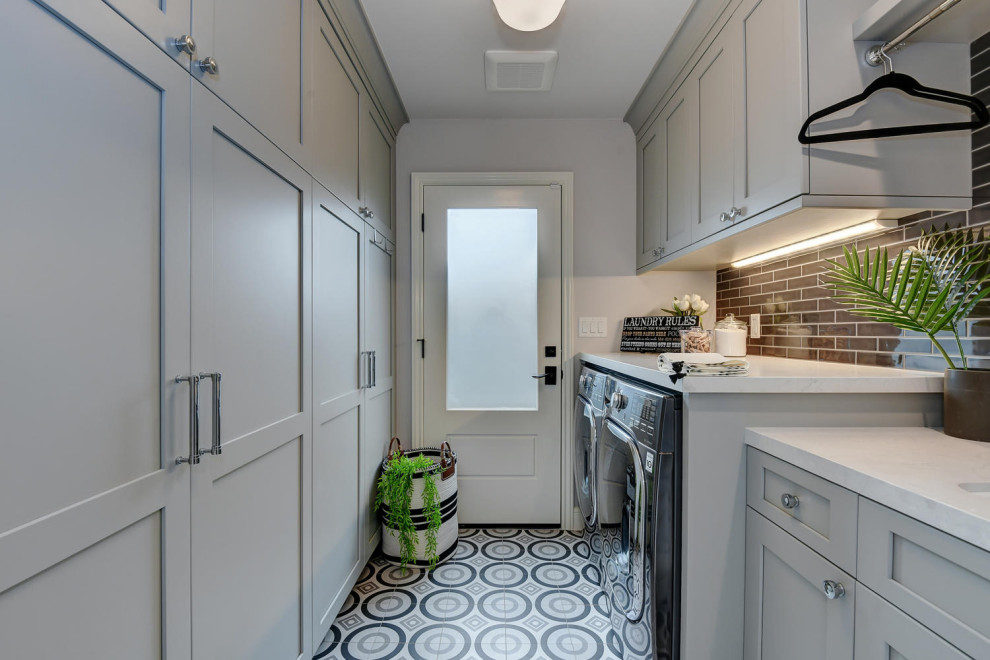 Mid-sized contemporary galley dedicated laundry room in San Francisco with raised-panel cabinets, an undermount sink, grey cabinets, quartz benchtops, grey walls, ceramic floors, a side-by-side washer and dryer, multi-coloured floor, grey benchtop, black splashback and glass sheet splashback.