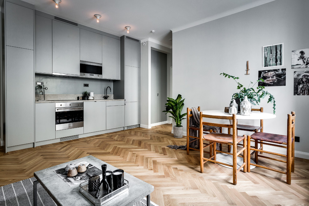 Design ideas for a large scandinavian single-wall open plan kitchen in Stockholm with flat-panel cabinets, grey cabinets, light hardwood floors, no island and grey splashback.