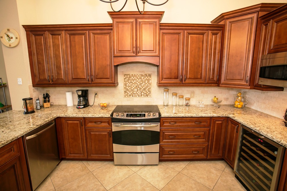 Example of a mid-sized transitional u-shaped porcelain tile eat-in kitchen design in Miami with an undermount sink, raised-panel cabinets, brown cabinets, granite countertops, beige backsplash, stone tile backsplash, stainless steel appliances, beige walls and a peninsula