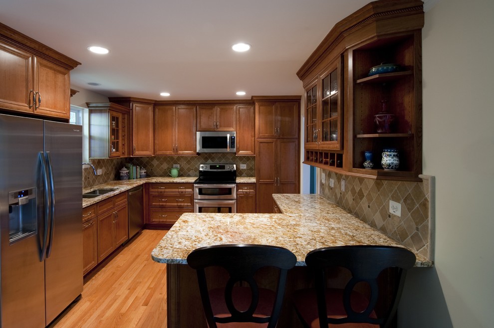 Photo of a large traditional l-shaped kitchen in DC Metro with a double-bowl sink, beaded inset cabinets, dark wood cabinets, granite benchtops, beige splashback, stone tile splashback, stainless steel appliances, medium hardwood floors and a peninsula.