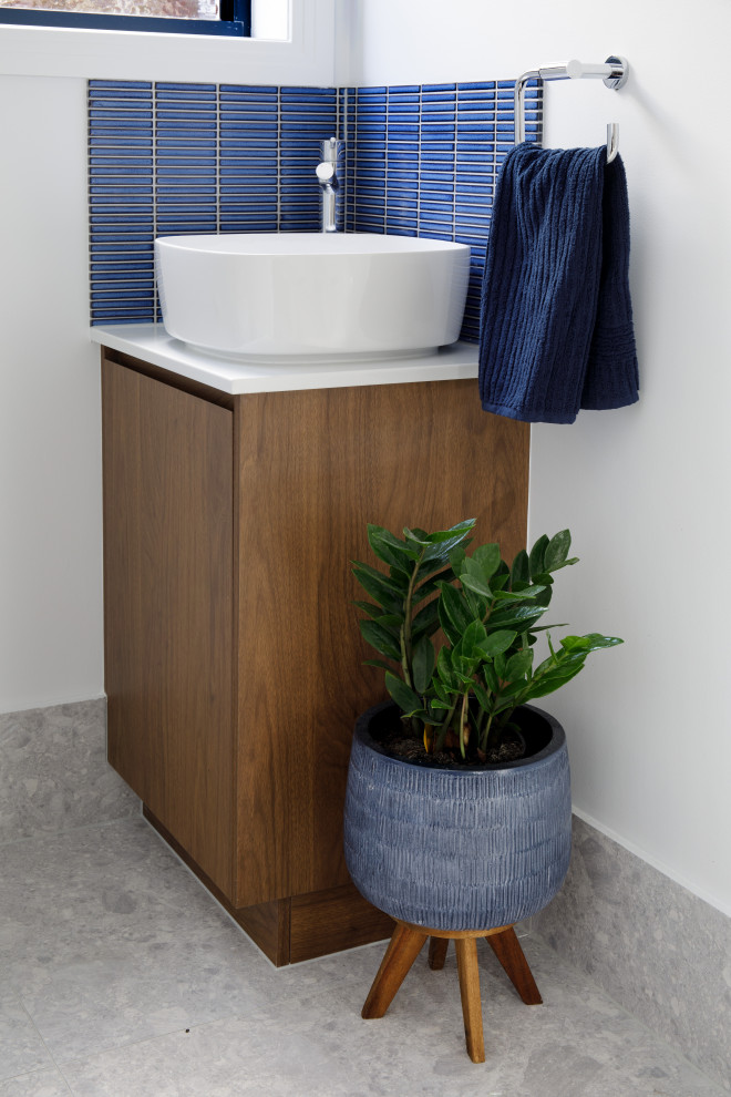 Inspiration for a small modern kids bathroom in Brisbane with flat-panel cabinets, medium wood cabinets, a corner tub, a two-piece toilet, blue tile, porcelain tile, white walls, porcelain floors, a vessel sink, engineered quartz benchtops, grey floor, white benchtops, an enclosed toilet, a single vanity and a built-in vanity.